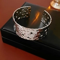 Macro detail of silver wide hollow cuff bracelet with hammer texture on black leather - Silver