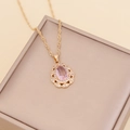Golden teardrop necklace with pink center stone and crystal halo on beige jewelry box - Pink