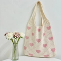 Beige knitted tote bag with pink heart pattern hanging on a white wall with roses - Apricot and Pink