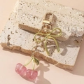 Sparkly pink cherry keychain with gold bow pendant on a beige stone background - Pink Glitter Cherry Gold Bow