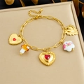 Dettaglio di un bracciale dorato con un cuore in gemma rossa e ciondoli a fungo - Braccialetto Pezzo Singolo (B1807) / Oro