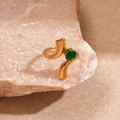 Macro-opname van gouden vortex ring met smaragdgroene steen op natuurlijke steenbasis - Groene Stroomlijn Spiraal