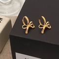 Close-up of golden bow-shaped ribbon earrings on a textured jewelry box background - Gold Bowknot Earrings