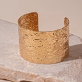 Detalle macro del brazalete ancho dorado con textura martillada sobre base de piedra - Dorado