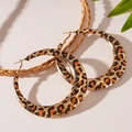Dettaglio di grandi orecchini a cerchio dorati con stampa animalier e foglie verdi - Cerchio Leopardato