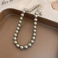 Élégant collier de perles gris-vert avec fermoir doré sur plateau marron au style minimaliste - 10mm / Gris