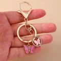 Porte-clés doré avec papillons roses en strass et fermoir à ressort sur fond beige - Rose Rouge