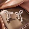 Detailed close-up of bow-shaped pearl earrings with gold-tone fringe on satin fabric - 1158-Bowknot Stud Earrings