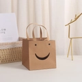 Close-up of brown kraft gift bag with smiley face cutout on a cozy white desk setup - Smiley Natural 10x10x10cm