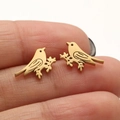 Golden bird stud earrings in stainless steel shown on fingertip for size scale - Gold