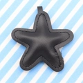 Black leather star keychain with visible stitching details on a striped background - Black