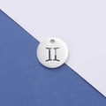 Macro shot of silver Gemini zodiac pendant with hollow geometric cutout on two-tone paper - Gemini
