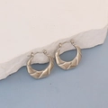 Detailed view of silver sculptural twisted hoop earrings resting on a white stone base - Silver Fluid Twisted Design