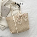 Beige Strohtasche mit weißer Spitzen-Schleife und Rosenstickerei auf einem Bett - Gebrochenes Weiß