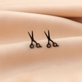 Detail shot of mini black scissor stud earrings on elegant champagne silk fabric - Black