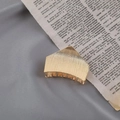 Close-up of a golden geometric metal hair claw clip placed on a vintage book - Brushed Gold Geometric