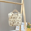 Waterproof baby bib with beige dinosaur and palm tree patterns hanging on a wooden hanger - Dinosaur Forest