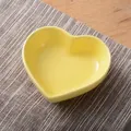 Bright yellow heart-shaped ceramic dipping dish for seasonings on a textured placemat - Yellow