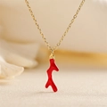 Elegant gold necklace with a vibrant red coral branch pendant on soft fabric - Red