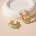 Detalle de pendientes en U de resina verde claro con forro de metal dorado en fondo beige - Hebilla de Oreja de Resina en Forma de U Verde