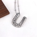Detail of silver U-shaped letter pendant with textured diamond faceted surface on white fabric - Letter U