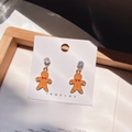 Dettaglio macro di orecchini a omino di pan di zenzero con smalto arancione e cristallo - Omino di pan di zenzero