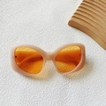 Eleganti occhiali da sole beige cat-eye con lenti arancioni su superficie bianca materica - Beige