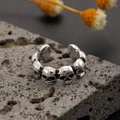 Macro shot of vintage silver skull ear cuff on grey rock with rustic punk details - Alloy / Triple Skull Ring / Antique Silver