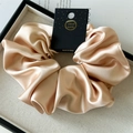 Detail of a luxury oversized champagne satin scrunchie with a handmade tag on a tray - 18cm / Khaki