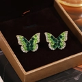 Close-up of golden butterfly earrings with green crystals and sparkling white rhinestones - Emerald Green Rhinestone Butterfly Gold Studs