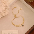 Dettaglio del bracciale regolabile a perline dorate con lettera U e occhio blu - Lettera U
