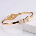 Bracciale rigido dorato con fiocco di zirconi brillanti su sfondo in marmo bianco - Braccialetto a Fiocco / Oro