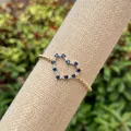 Macro view of gold-plated heart bracelet featuring blue zircons on beige linen roll - Gold/Blue Zirconia