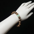 Minimalist sandalwood bead bracelet with green jade stone accent on a female wrist - Gold Silk Sandalwood 10mm With Green Jade