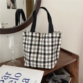 Detail of checkered tote bag with golden clasp on a rustic wooden shelf setting - Black Small Plaid Woolen