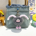 Cute grey plush monster keychain with pink horns hanging on a light blue denim bag - Gray