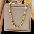 Polished gold woven wheat chain necklace in stainless steel shown on jewelry display - Flower Basket Chain Necklace / Gold