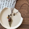 Collier bohème avec plumes en bronze et perles de bois sur une assiette en céramique - Grande Plume Dorée