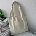 Minimalist beige canvas tote bag with outer pocket shown in a cozy interior setting - Off White