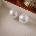 Macro shot of a smooth white round pearl earring set on a beige velvet jewelry box - White