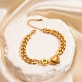 Golden stainless steel chain bracelet with textured heart and star charms on stone surface - Gold