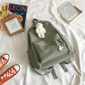 Detail of a sage green canvas backpack with plush bear charm and cute badges in a cozy setting - Green with Pins and Bear Pendant