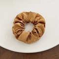 Detailed view of a gold satin scrunchie with silky pleated texture on a white plate - Large / Brown