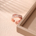 Gros plan d'une bague croisée en or rose avec zircons brillants sur fond doux neutre - Design Croisé Multi-boucles / Or rose