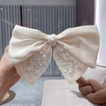 Macro detail of elegant cream satin bow hair clip with mesh and faux pearl accents - Beige