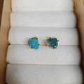 Detail of blue natural stone stud earrings with golden four-claw setting on display - Apatite