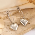 Macro detail of 3D puffy heart charms on polished silver hoops over stone and fabric - Silver Heart Hoop Earrings (2.9cm)