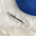 Dettaglio del fermaglio per capelli marmorizzato blu e bianco su carta bianca operata - Fermaglio a molla lungo
