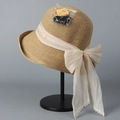 Detail van strooien zonnehoed met lint, parels en UPF 50+ zonbeschermingslabel - Beige Strik