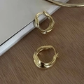 Close-up of golden wave geometric earrings on wood surface with polished finish - Streamlined Wave Hoop / Gold